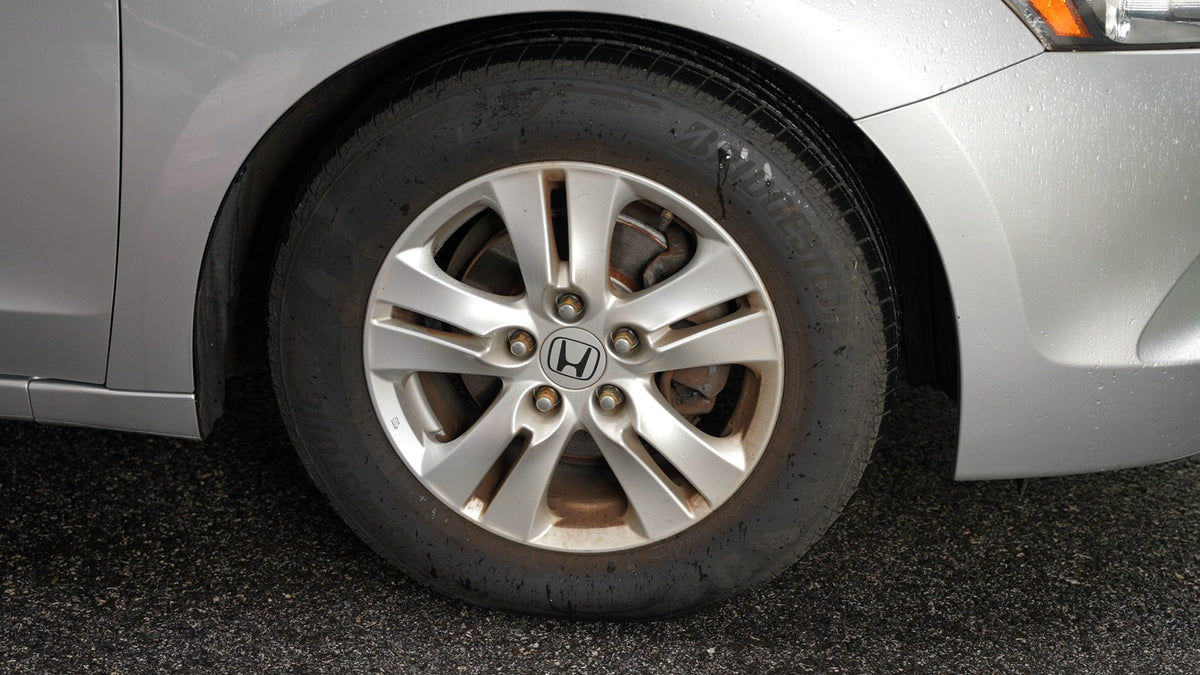 A silver Honda's front wheel, brown with brake dust
